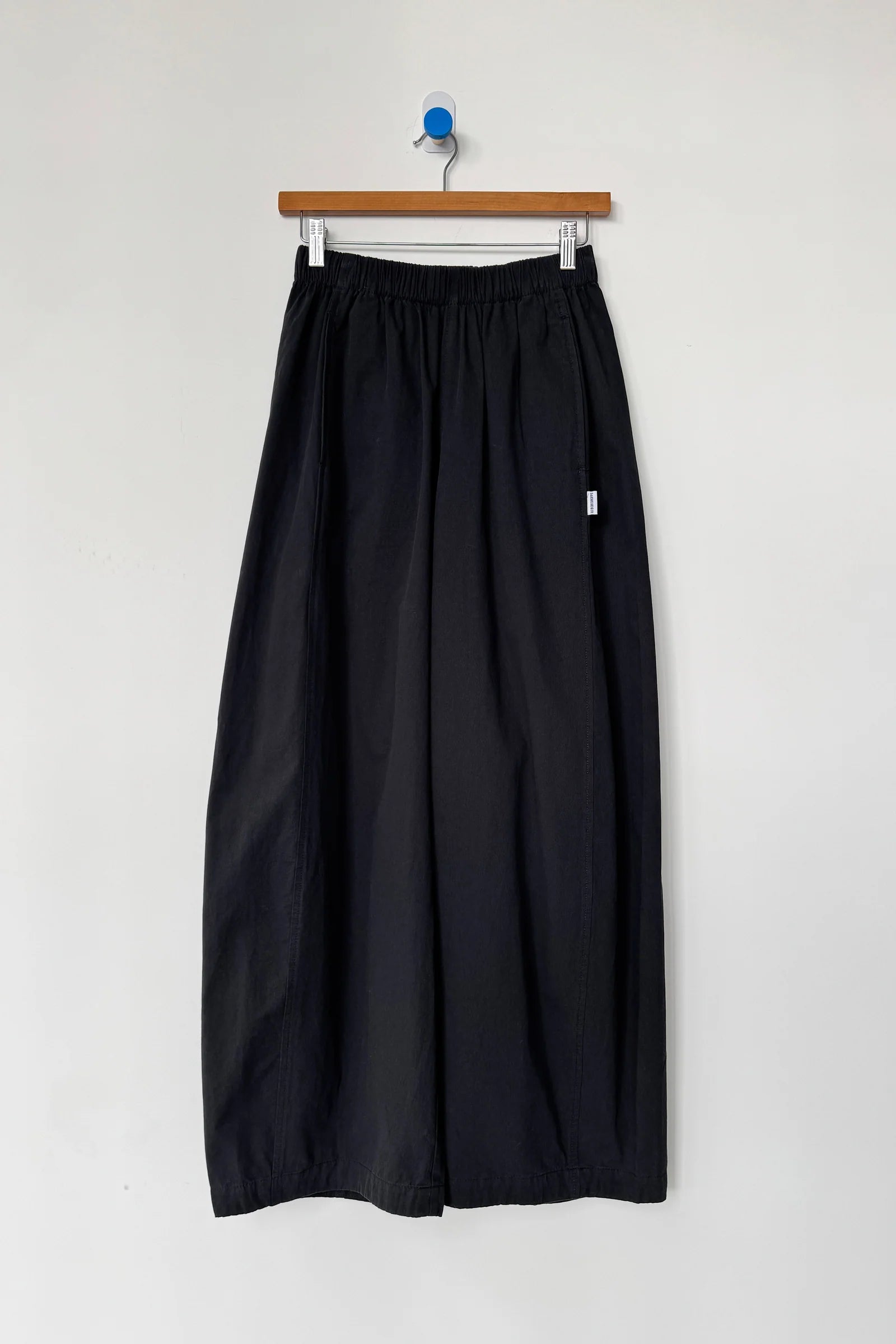 Black skirt hanging on a wooden hanger against a white wall