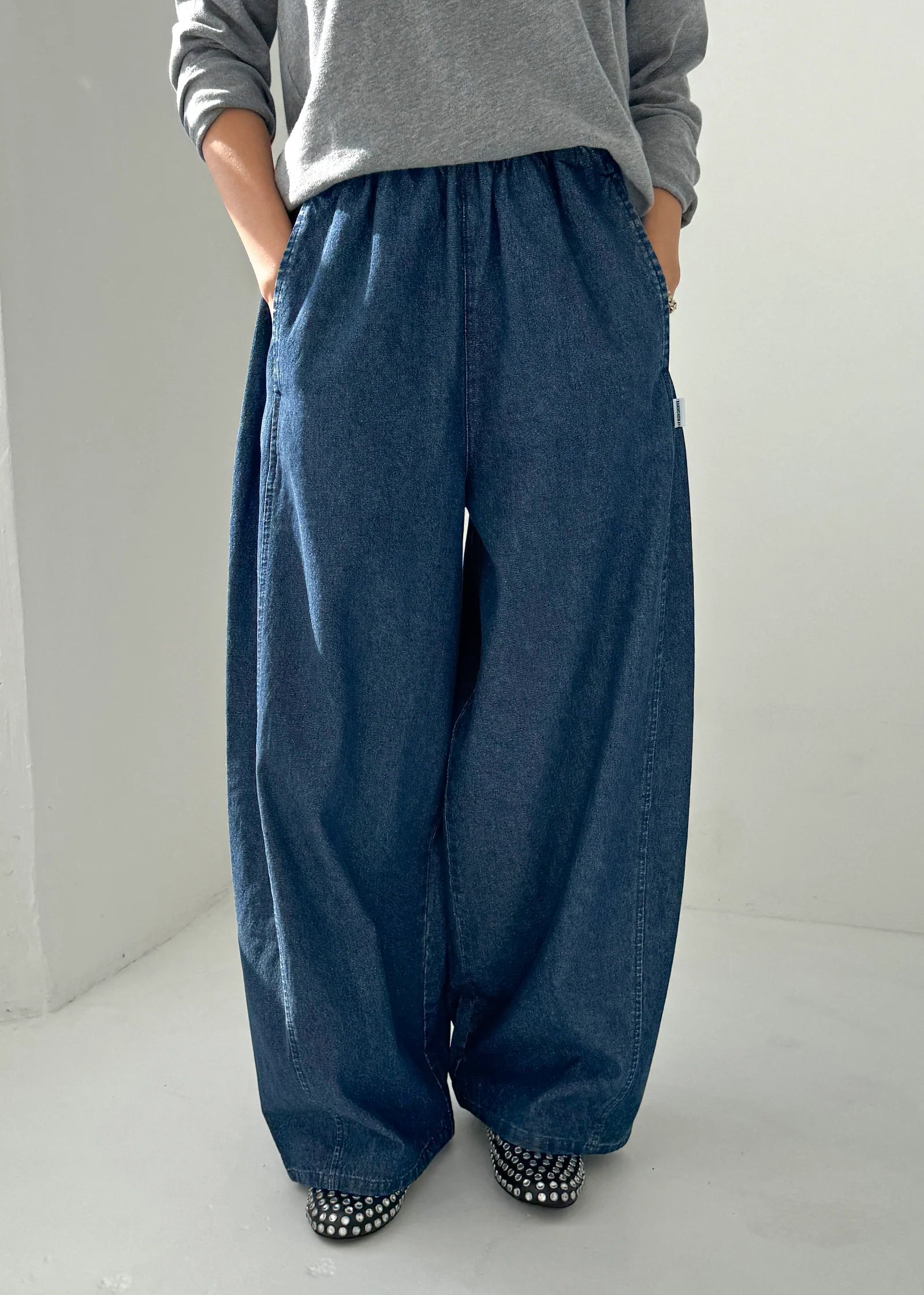 Person wearing blue wide-leg pants and a gray top on a plain background