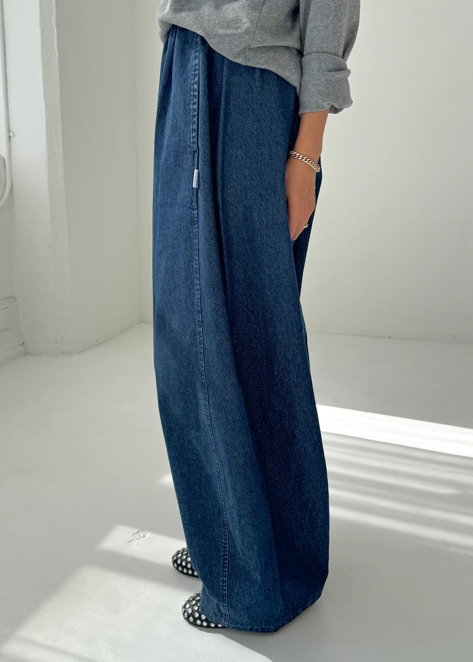 Person wearing blue wide-leg jeans and a gray top on a white background