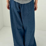 Person wearing a gray sweatshirt and blue wide-leg jeans on a white background