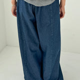 Person wearing a gray sweatshirt and blue wide-leg jeans on a white background