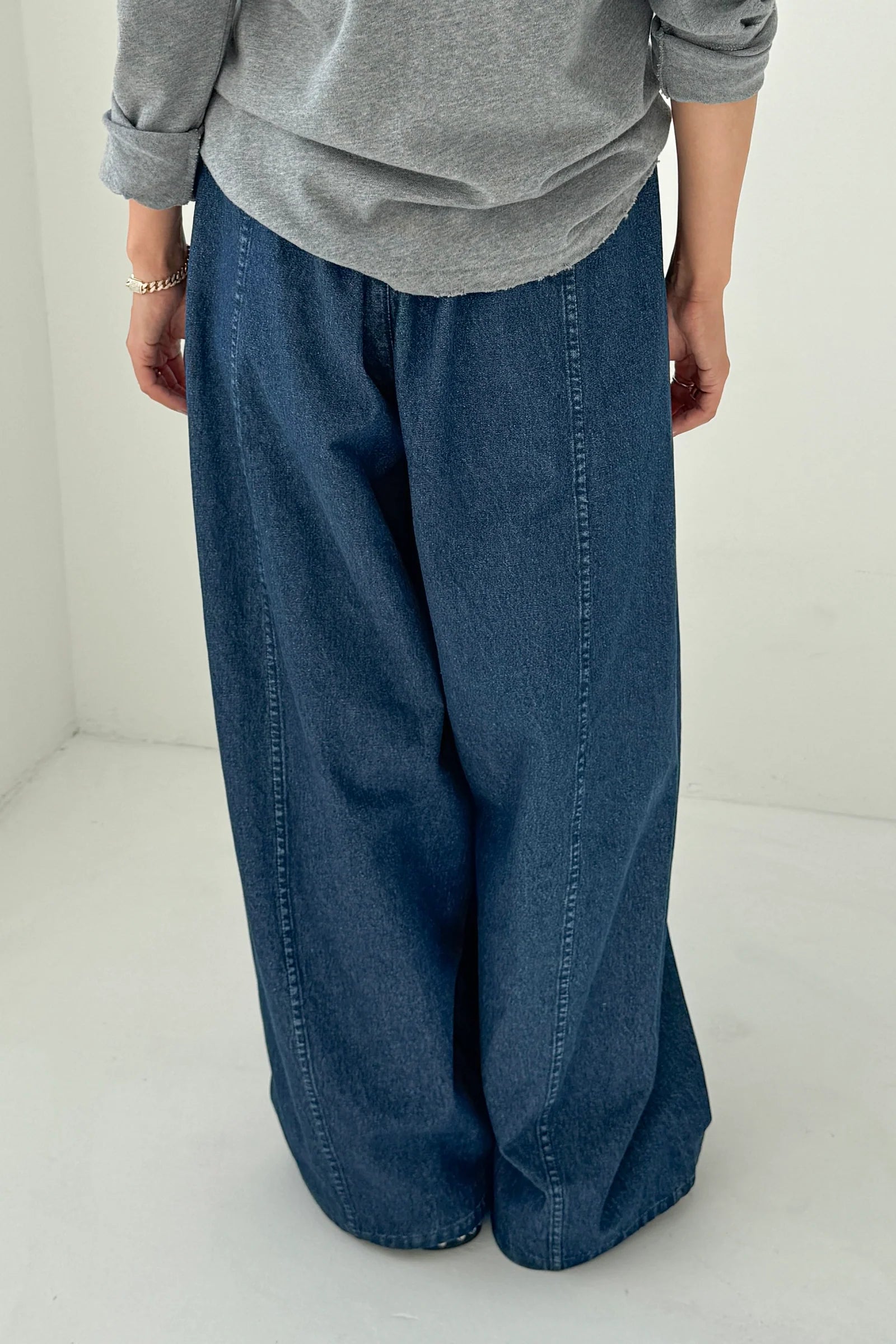 Person wearing a gray sweatshirt and blue wide-leg jeans on a white background