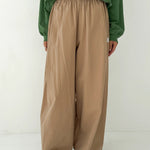 Person wearing a green top and beige wide-leg pants on a white background