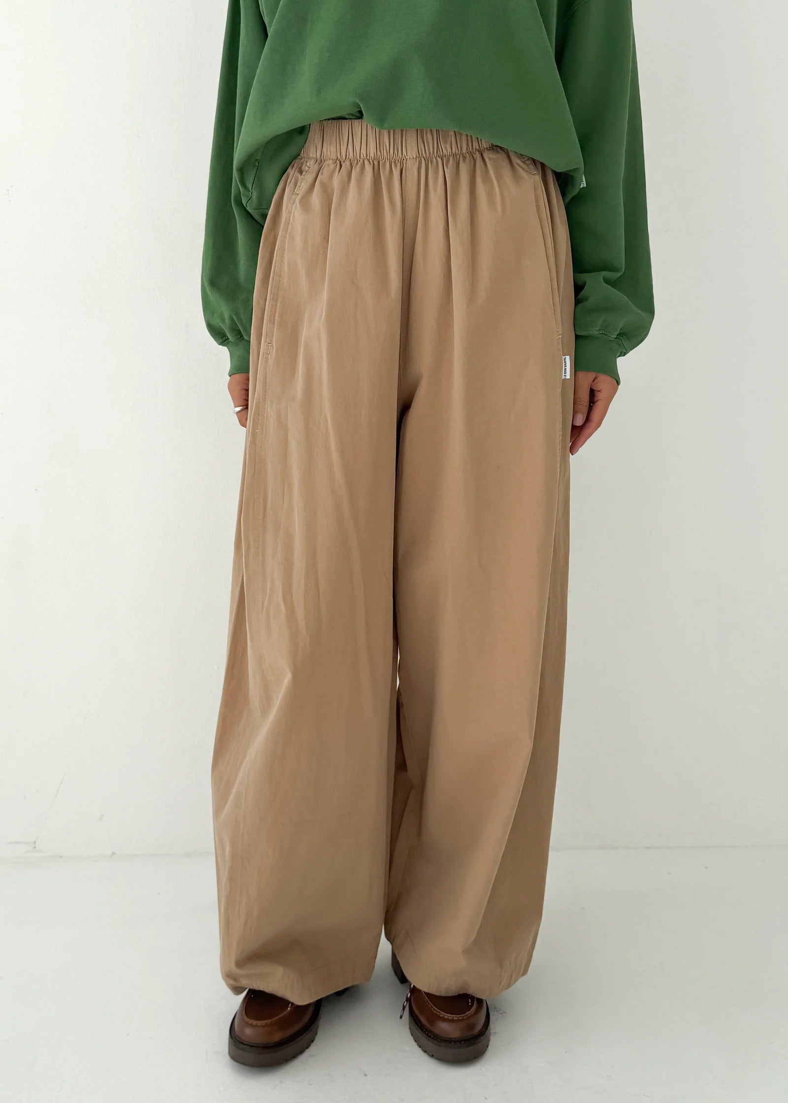 Person wearing a green top and beige wide-leg pants on a white background