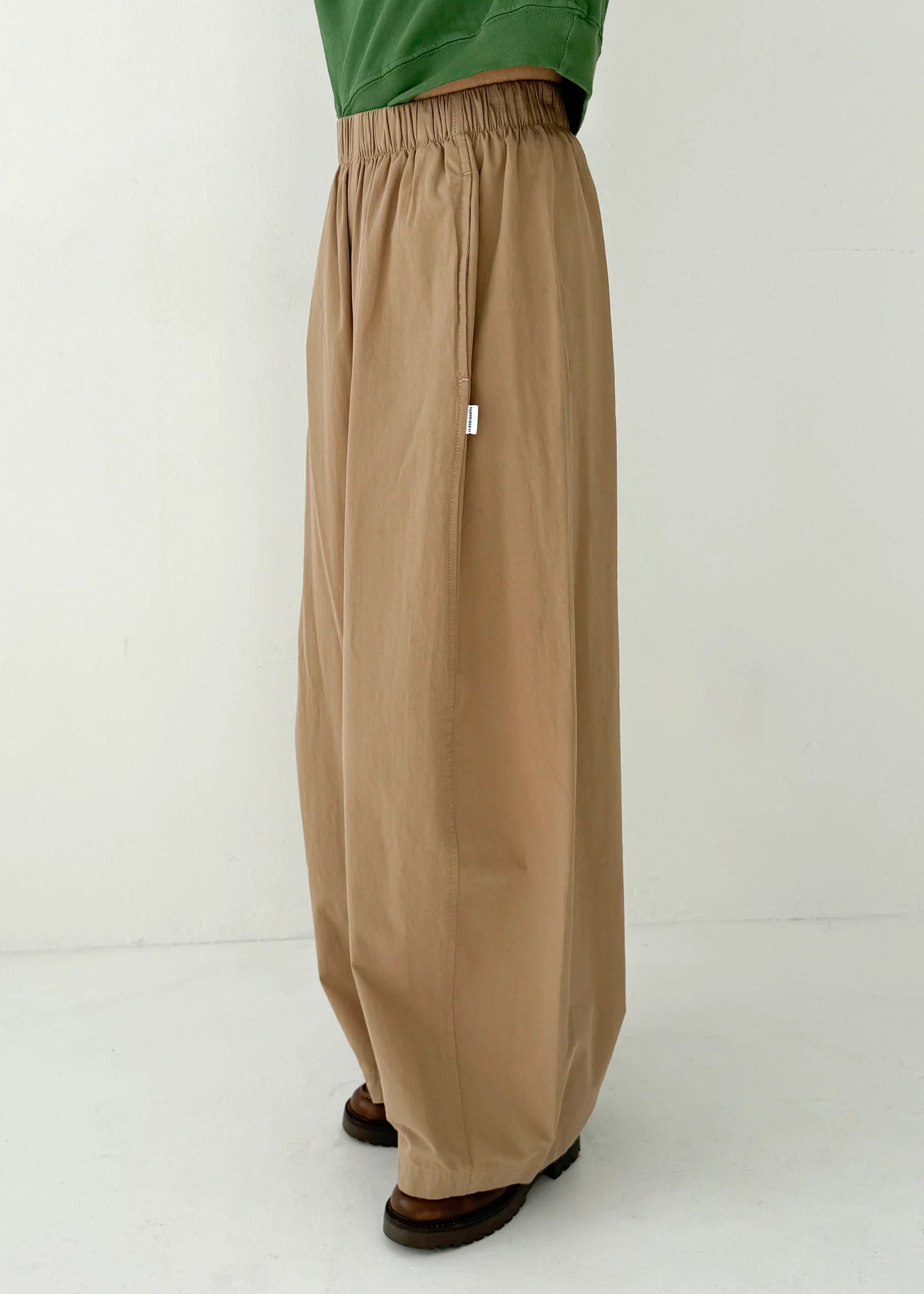 Person wearing beige wide-leg pants and a green top on a white background