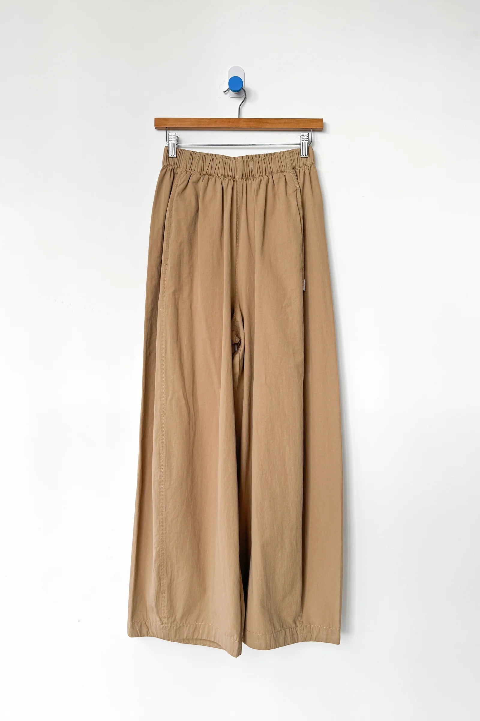 Beige pants hanging on a wooden hanger against a white background