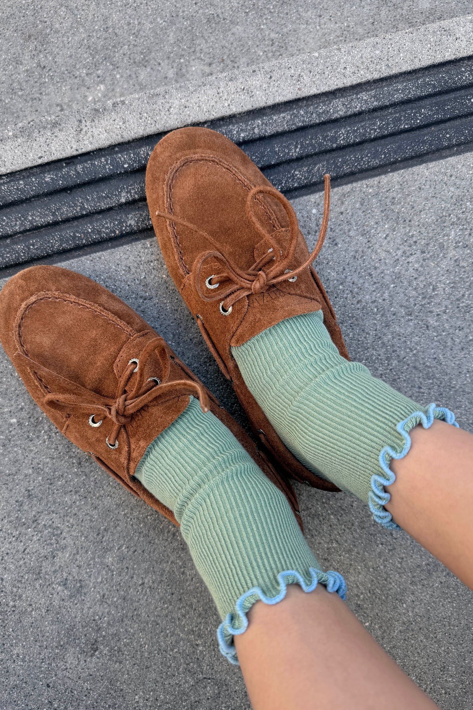 Brown suede loafers with green socks on a concrete surface