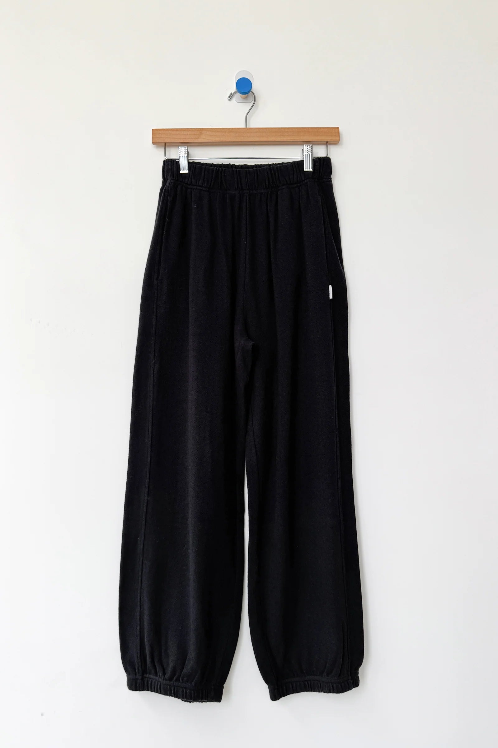 Black pants hanging on a wooden hanger against a white background