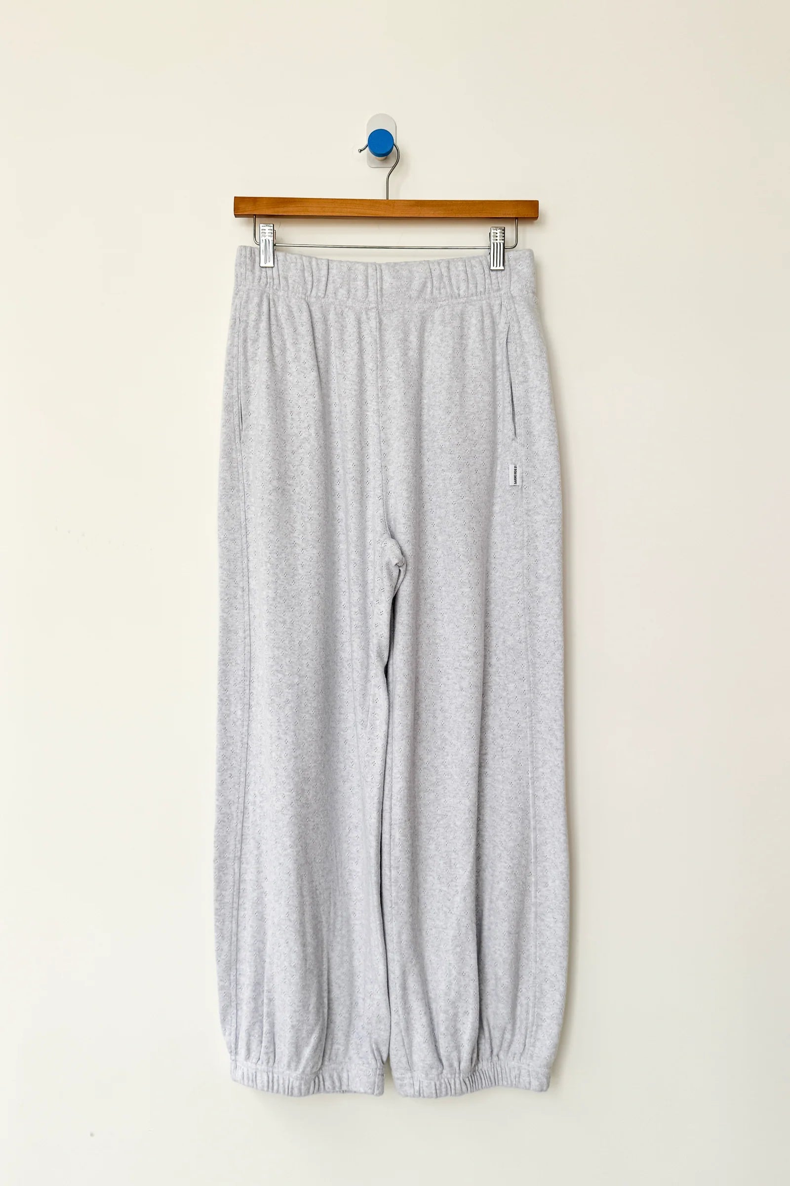 Gray pants hanging on a wooden hanger against a white wall