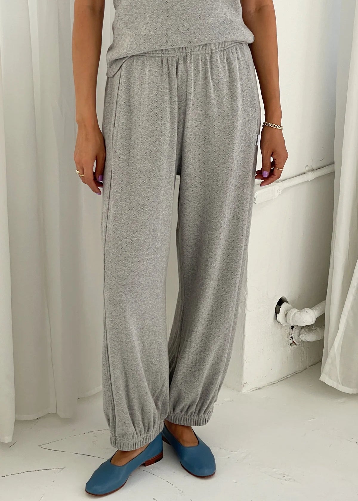 Person wearing gray sweatpants and blue shoes in a minimal indoor setting