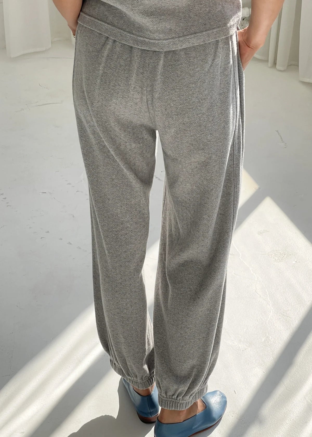 Person wearing gray sweatpants and blue shoes on a white floor.