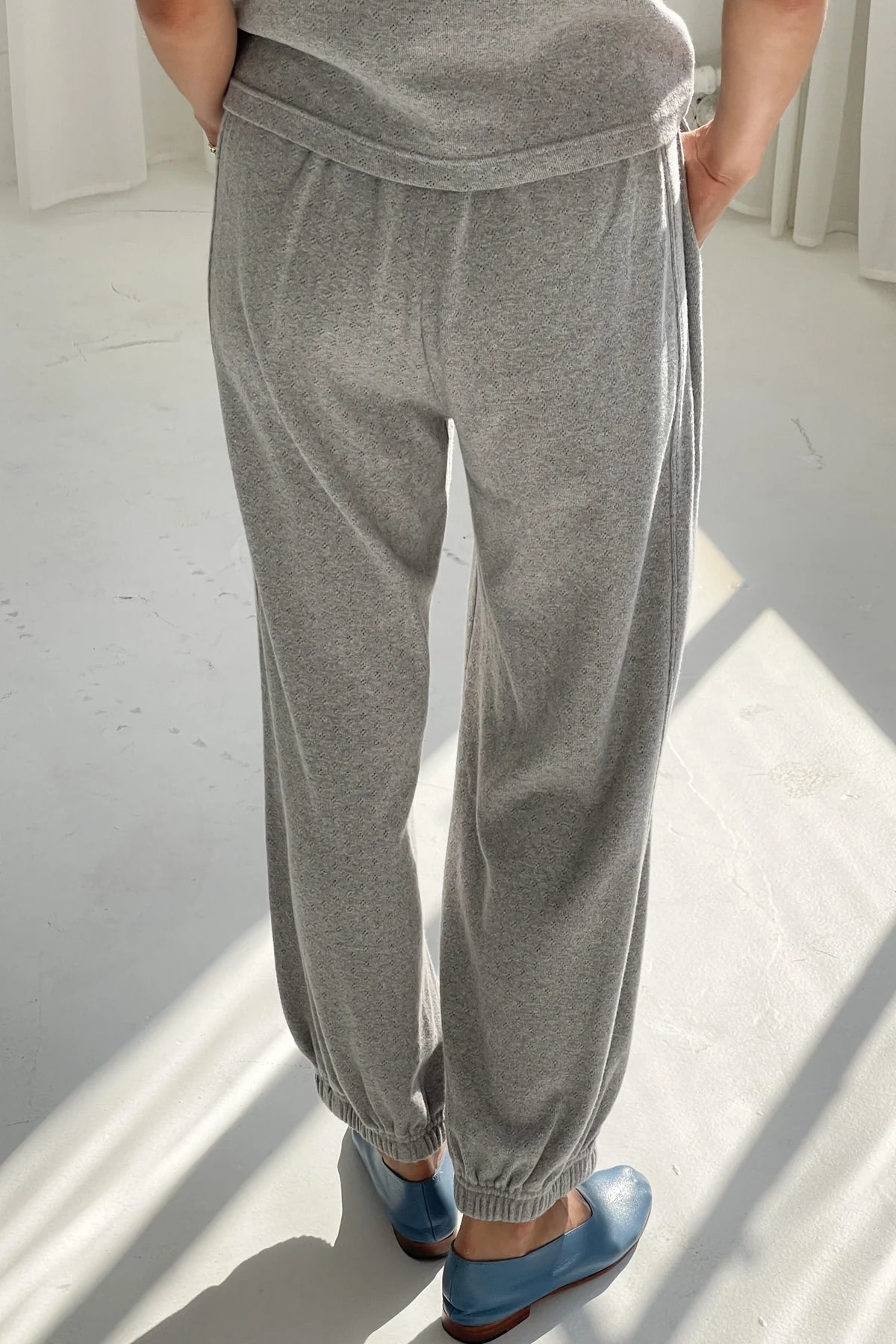 Person wearing gray sweatpants and blue shoes on a white floor.