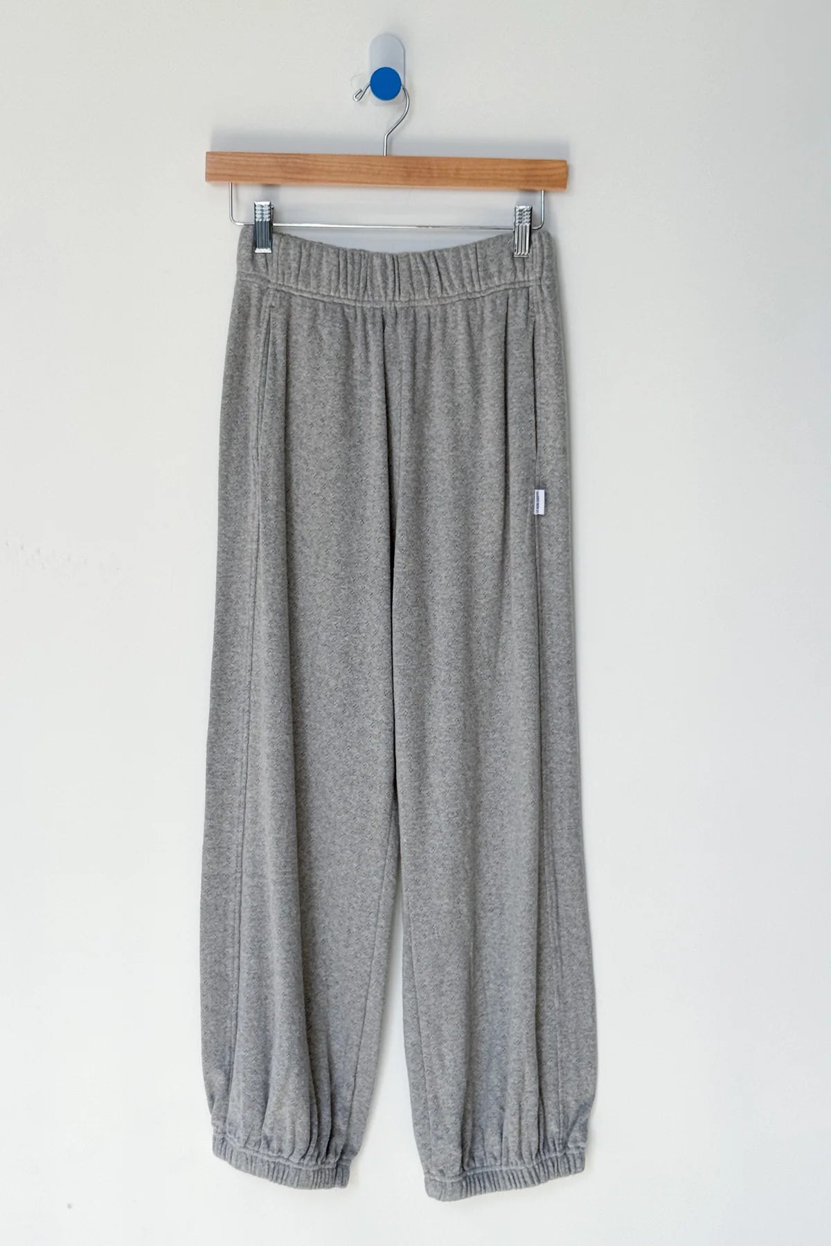 Gray sweatpants hanging on a wooden hanger against a white background
