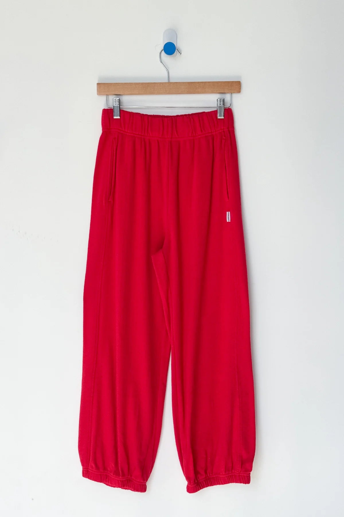 Red pants hanging on a wooden hanger against a white background