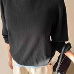 Person wearing a black sweater and beige pants holding a black handbag indoors.