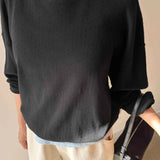Person wearing a black sweater and beige pants holding a black handbag indoors.