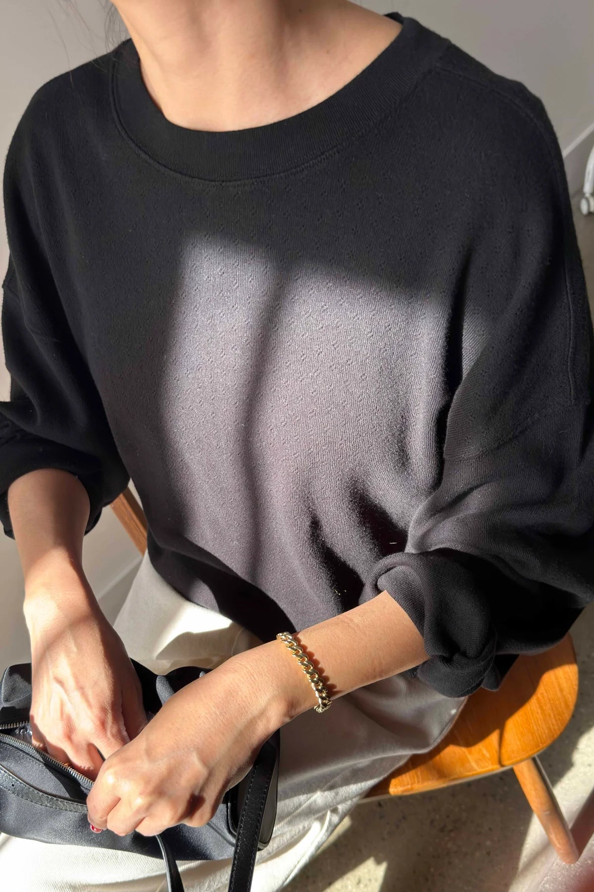 Person wearing a black sweatshirt sitting on a chair with a neutral background