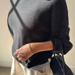 Person wearing a dark gray sweater holding a black handbag indoors.