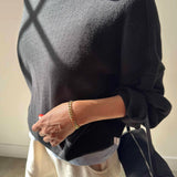 Person wearing a dark gray sweater holding a black handbag indoors.