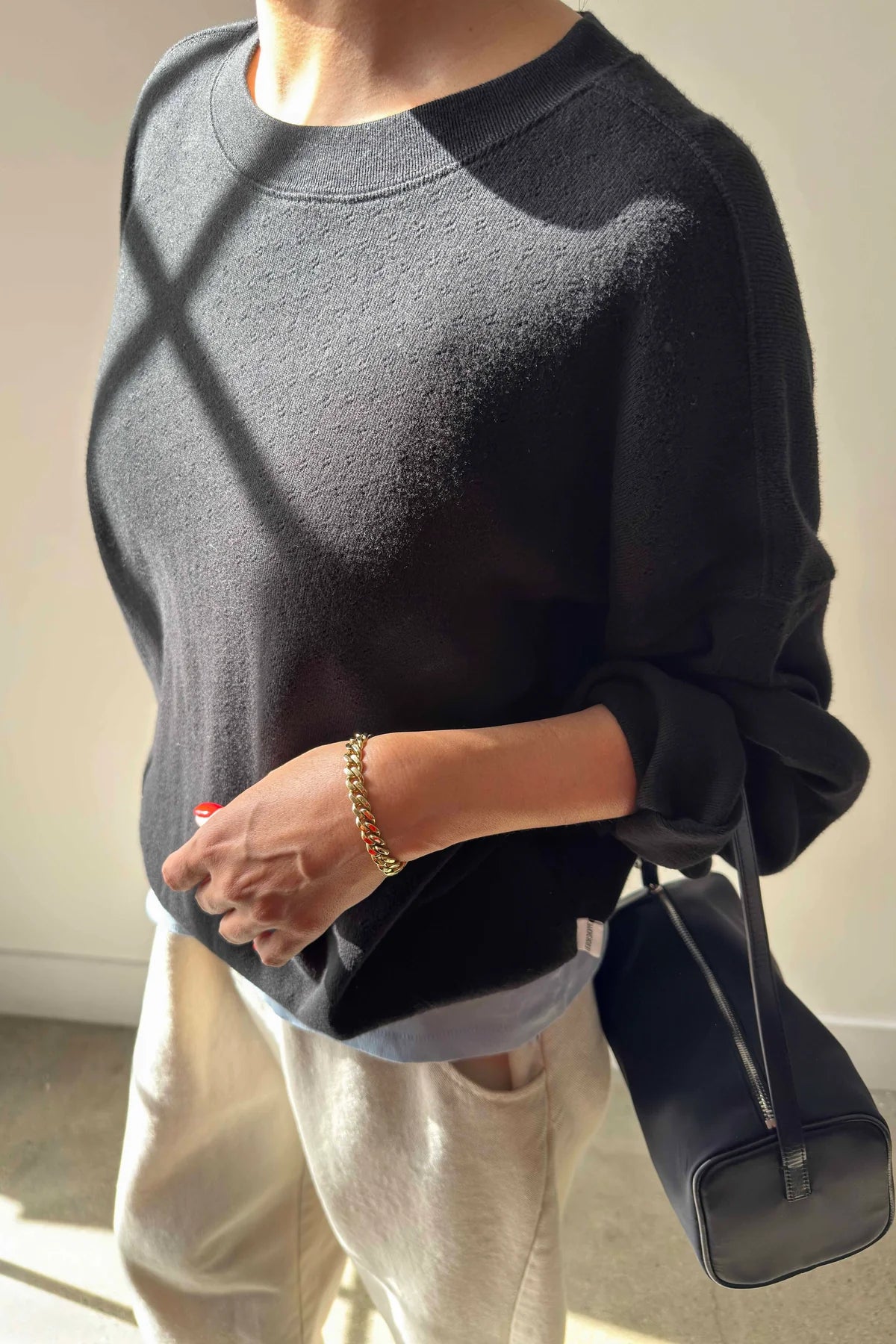 Person wearing a dark gray sweater holding a black handbag indoors.