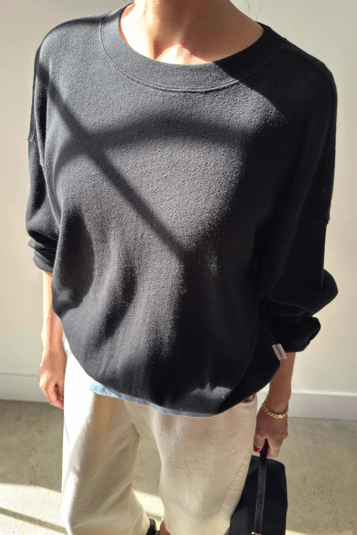 Person wearing a black sweater and light-colored pants indoors.