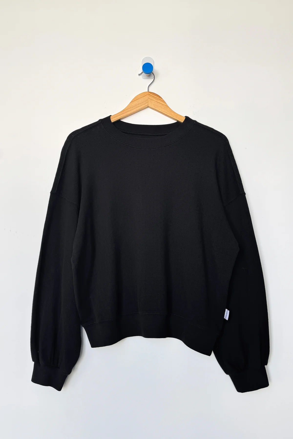 Black sweatshirt on a wooden hanger against a white background
