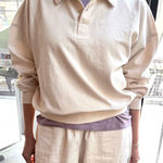 Person wearing a beige long-sleeve shirt and pants in an indoor setting
