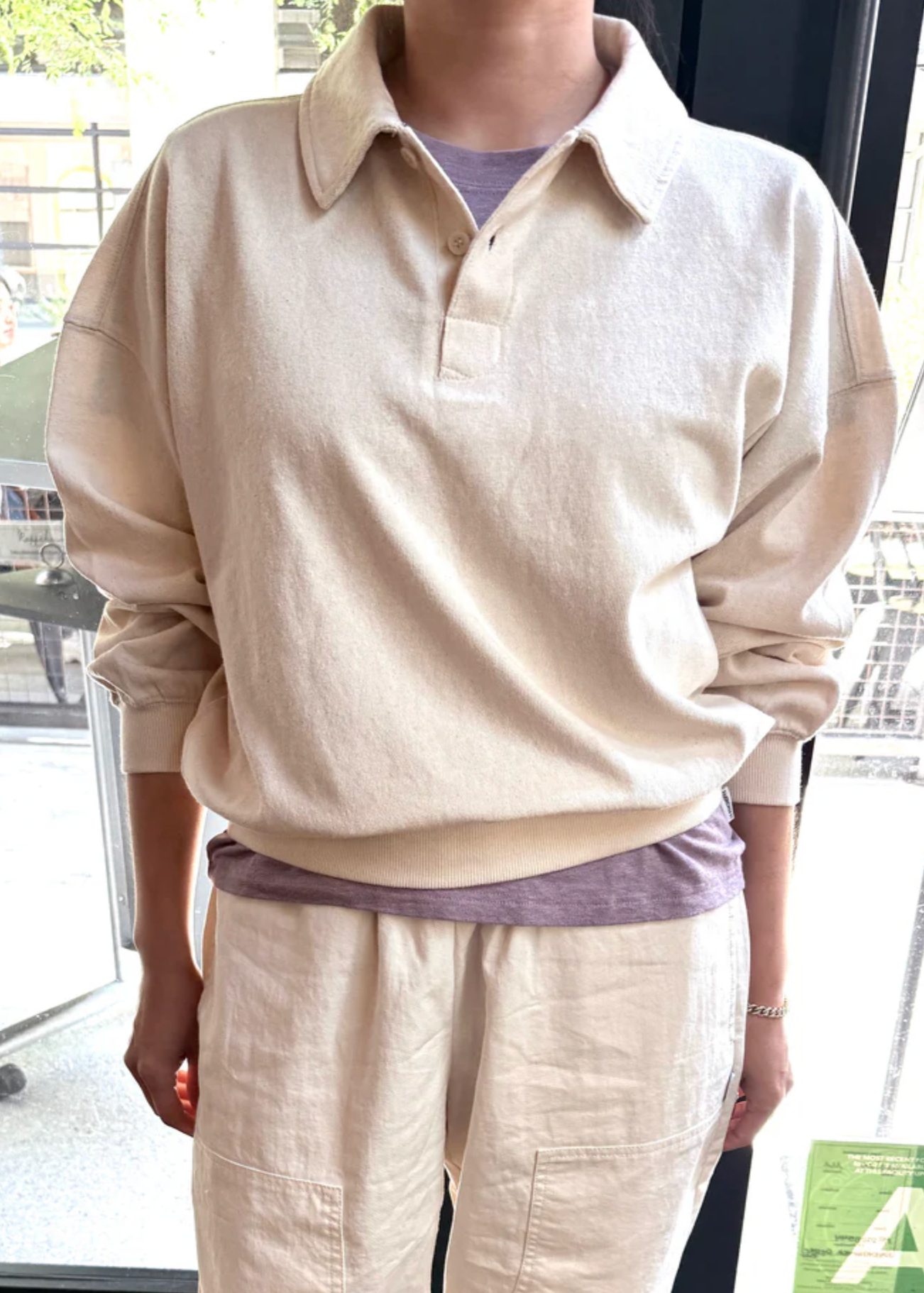 Person wearing a beige long-sleeve shirt and pants in an indoor setting