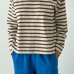 Person wearing a brown and white striped shirt with blue pants on a plain background