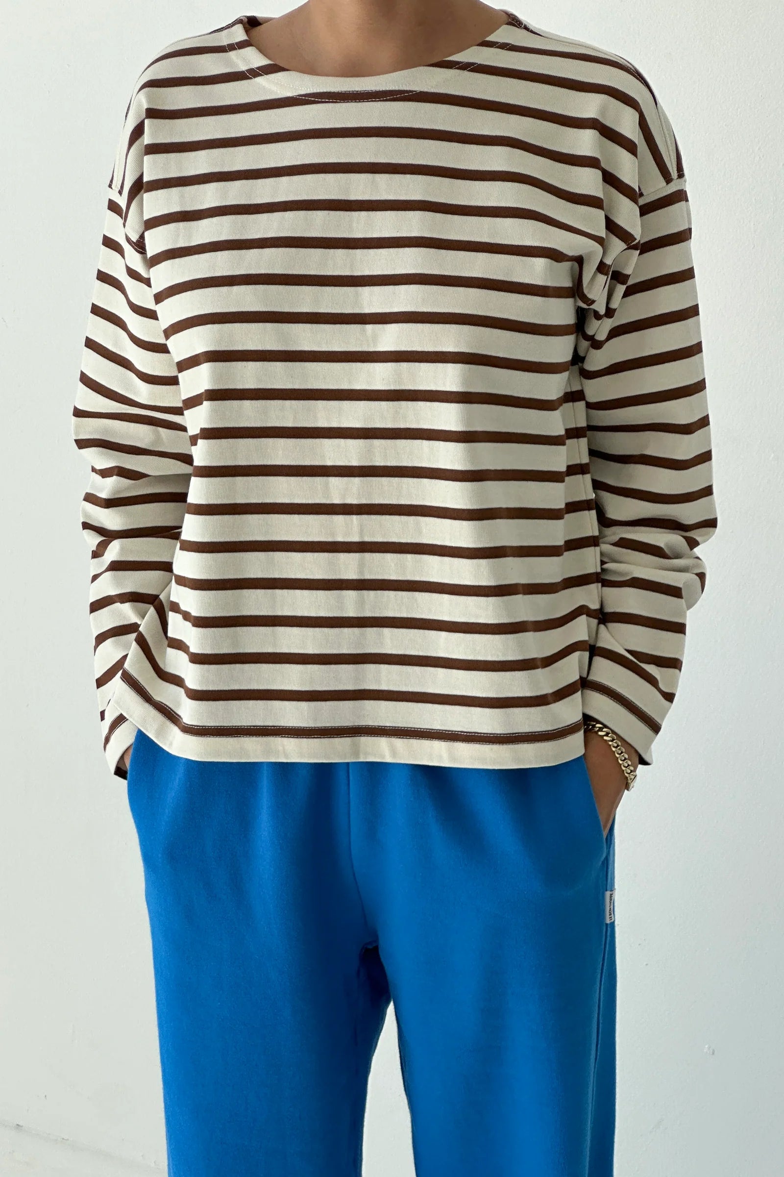 Person wearing a brown and white striped shirt with blue pants on a plain background