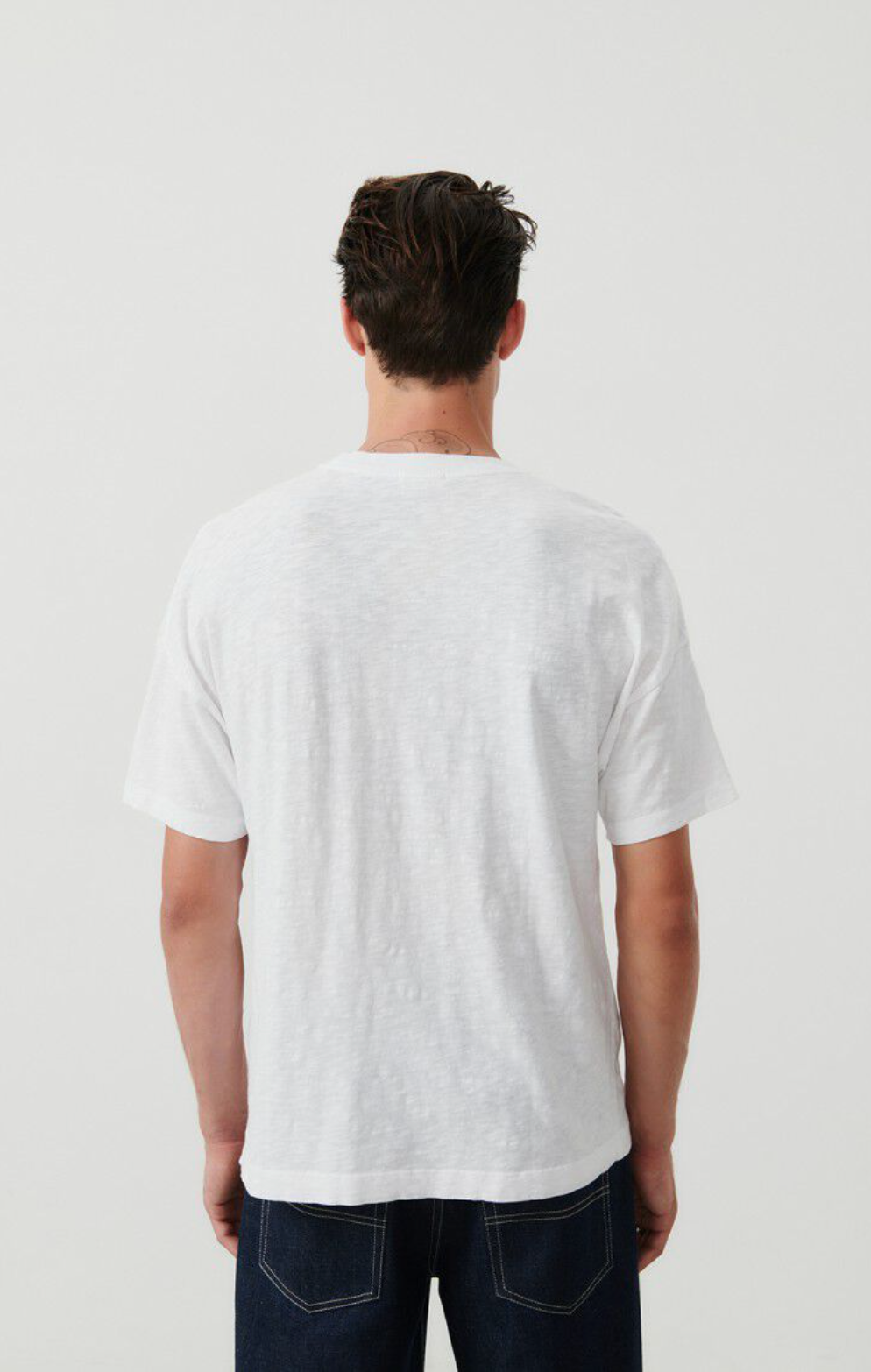 A medium close up backside image of a male model wearing the Bysapick T-Shirt in white styled with dark denim