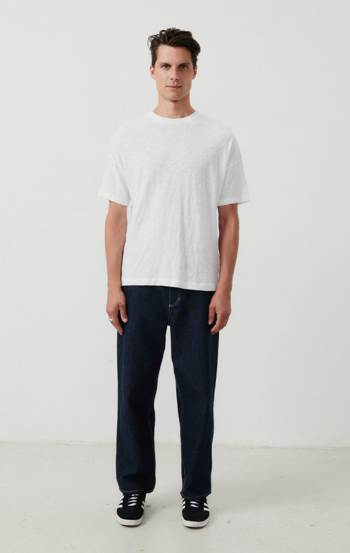 A full body front image of a male model wearing the Bysapick T-Shirt in white styled with dark denim and black sneakers
