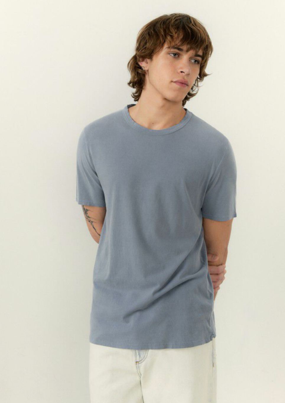 A medium close image of a male model wearing the devon tee shirt in vintage blue with white denim 