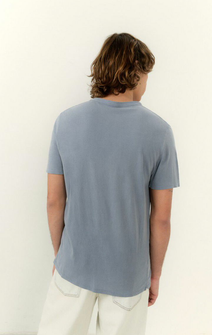 A medium close image of the backside of a male model wearing the devon tee shirt in vintage blue with white denim 