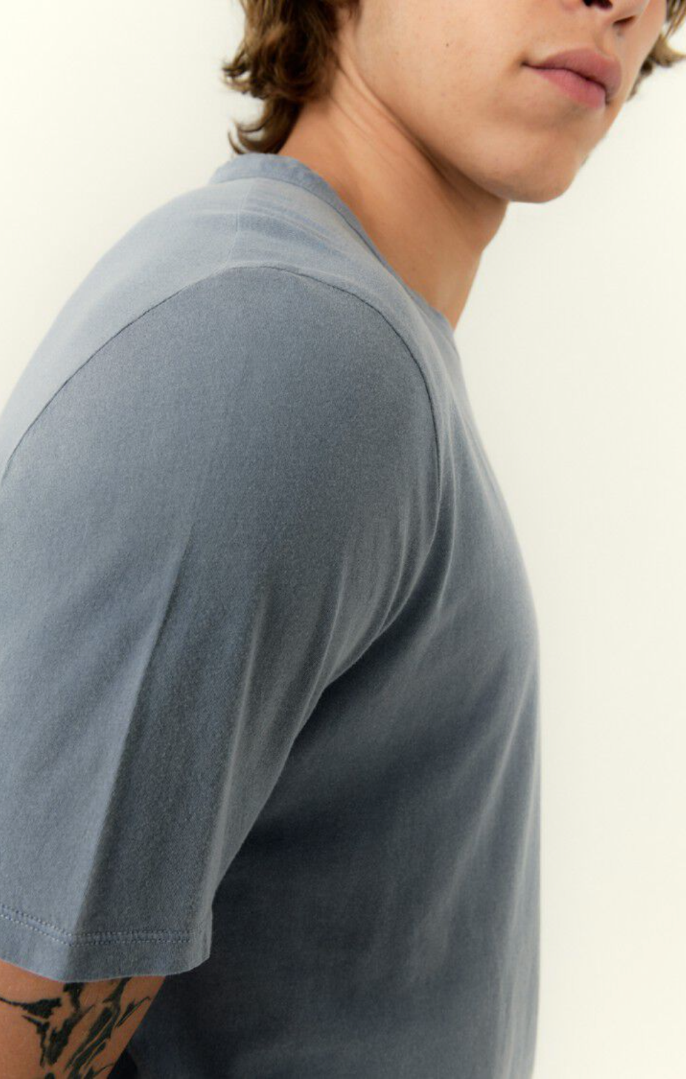 A close up shoulder detail image of a male model wearing the devon tee shirt in vintage blue with white denim 