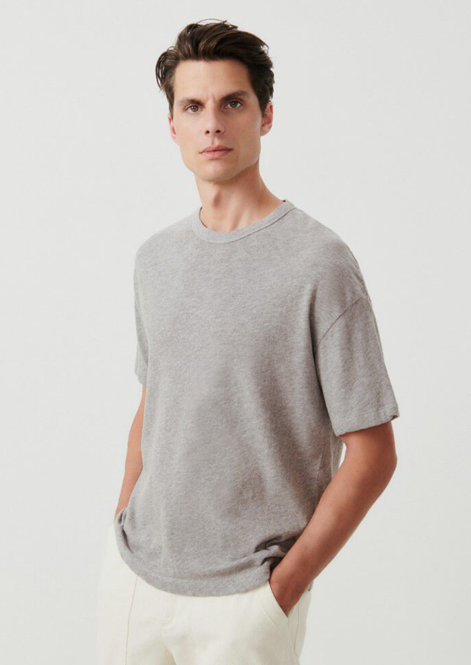 A medium close up image of a male model standing at an angle and with his hands in his pockets, wearing the Sonoma T-shirt in grey