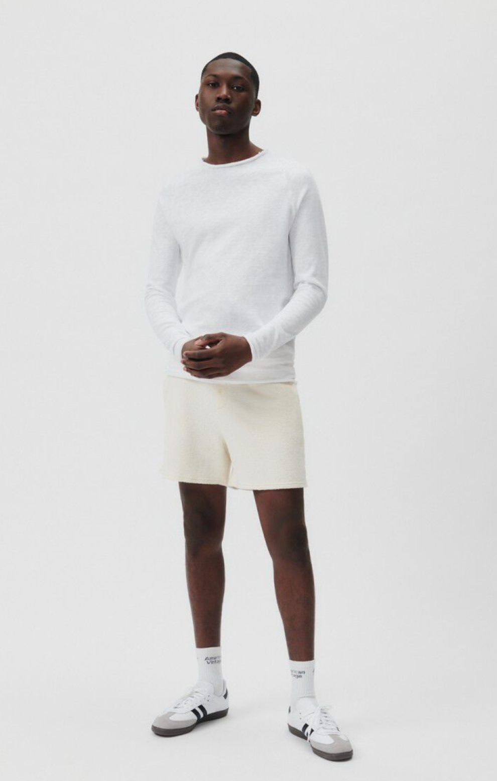 A full front body image of a male model wearing the Sonoma Long Sleeve in white styled with cream shorts and white sneakers