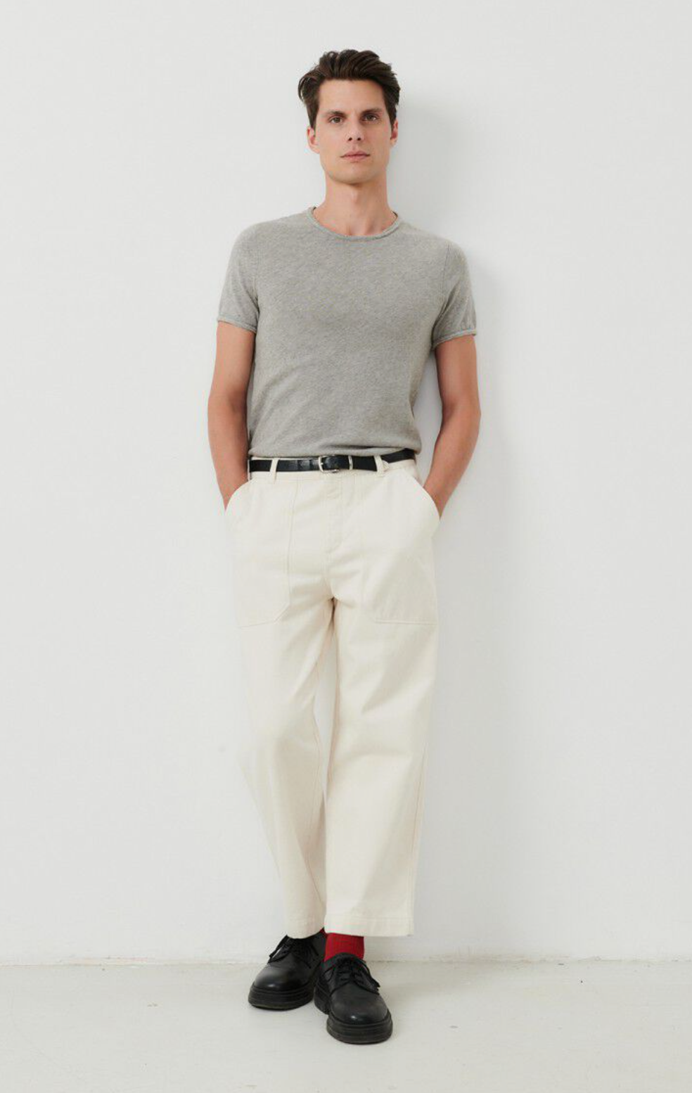 A full body image of a male model wearing the Sonoma tee shirt in grey tucked into white denim 