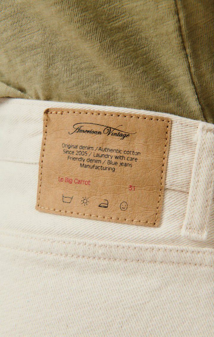 A close up detail image of the sewn on brand tag on the back waist of the Big Carrot Jeans in ecru