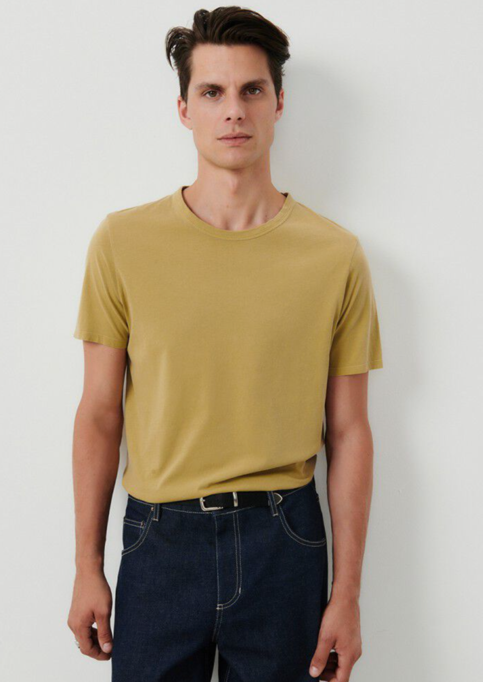 medium close image of a male model wearing the devon t-shirt in vintage safari, tucked into  dark denim