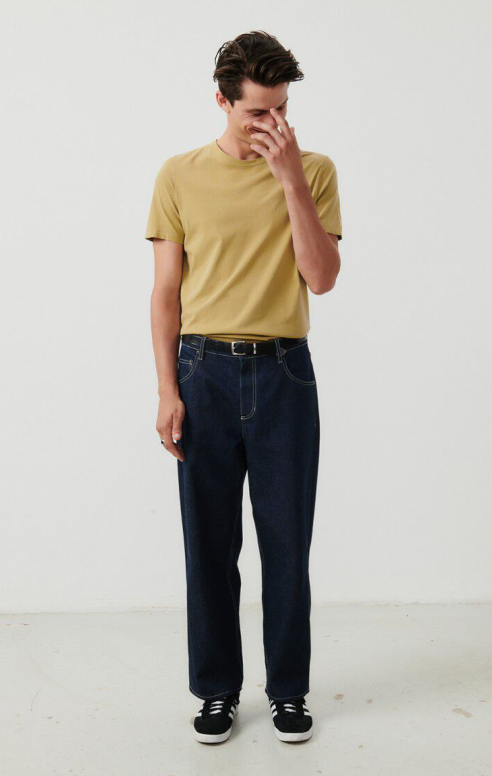 A full body front facing image of a male model wearing the Devon t-shirt in vintage safari tucked into dark denim