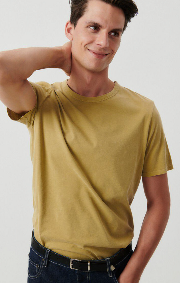 A medium close facing image of a male model wearing the Devon t-shirt in vintage safari tucked into dark denim