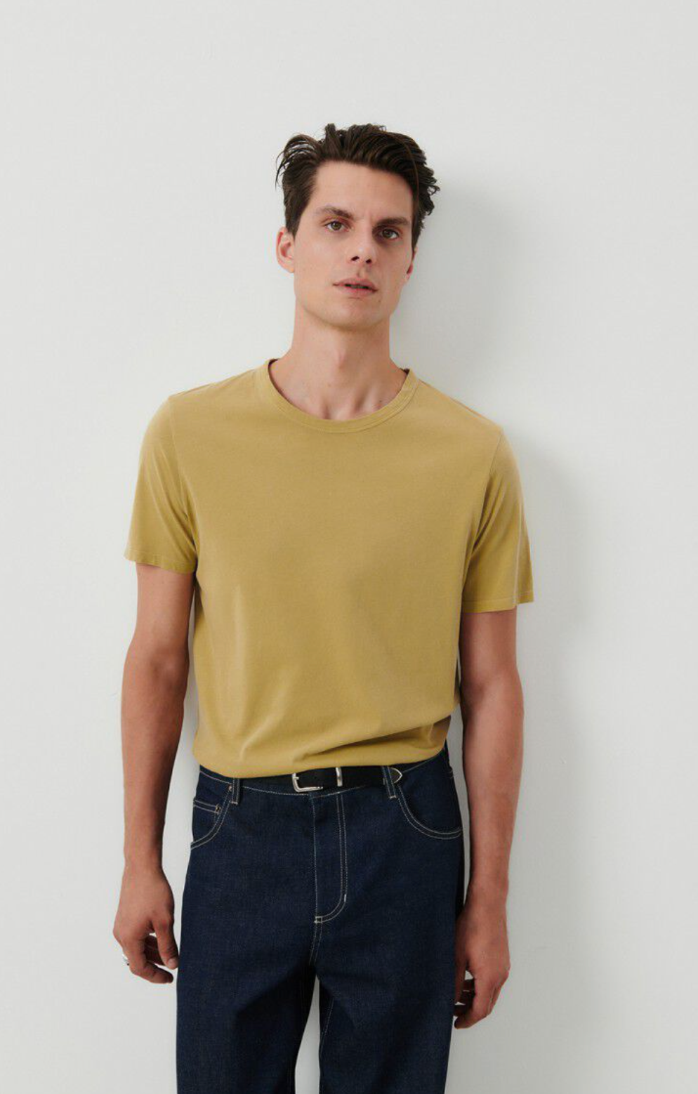 A medium close front facing image of a male model wearing the Devon t-shirt in vintage safari tucked into dark denim