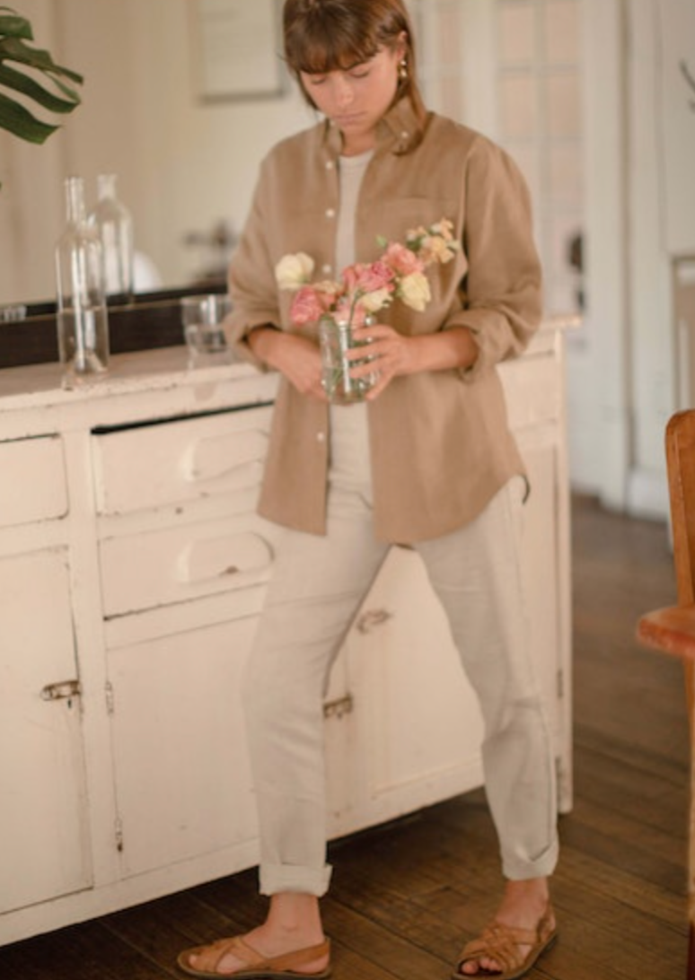 Image showing a female wearing the women's Playa Shirt in chai while standing in a home setting holding a vase of flowers. 