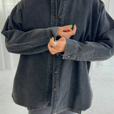 Person wearing an oversized black denim shirt with a blurred background