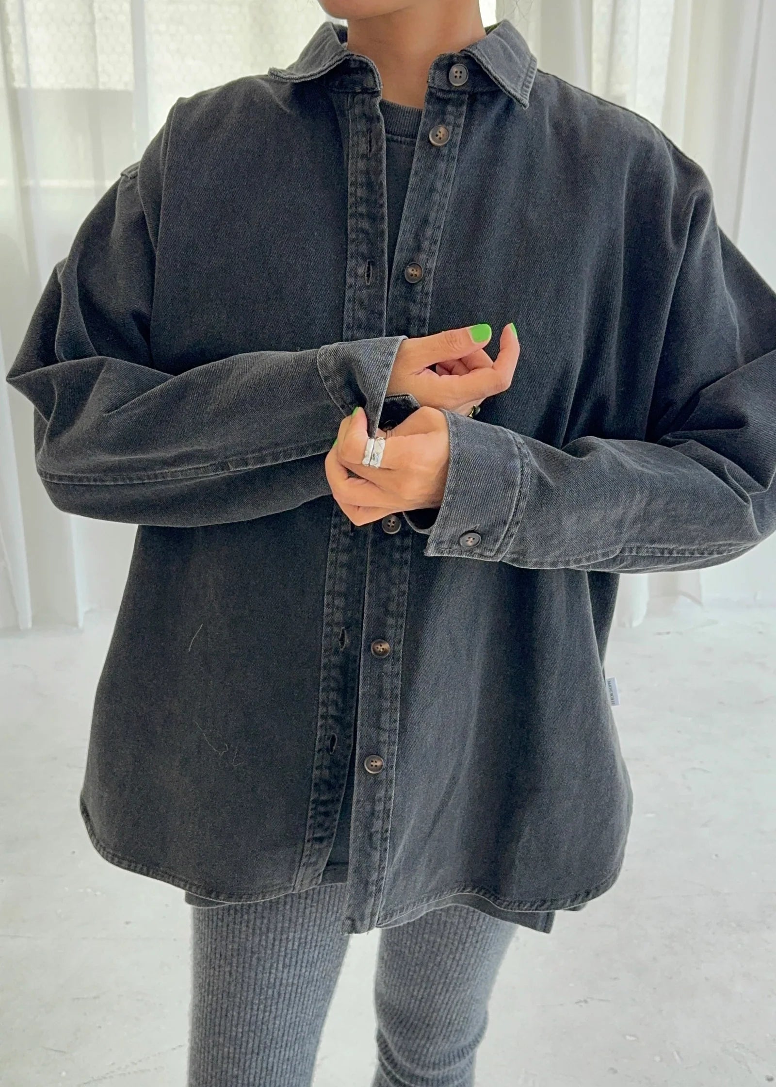 Person wearing an oversized black denim shirt with a blurred background