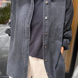 Person wearing a dark denim shirt over a black t-shirt with beige pants, standing indoors.