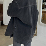 Person wearing a dark denim jacket and gray pants in an indoor setting.