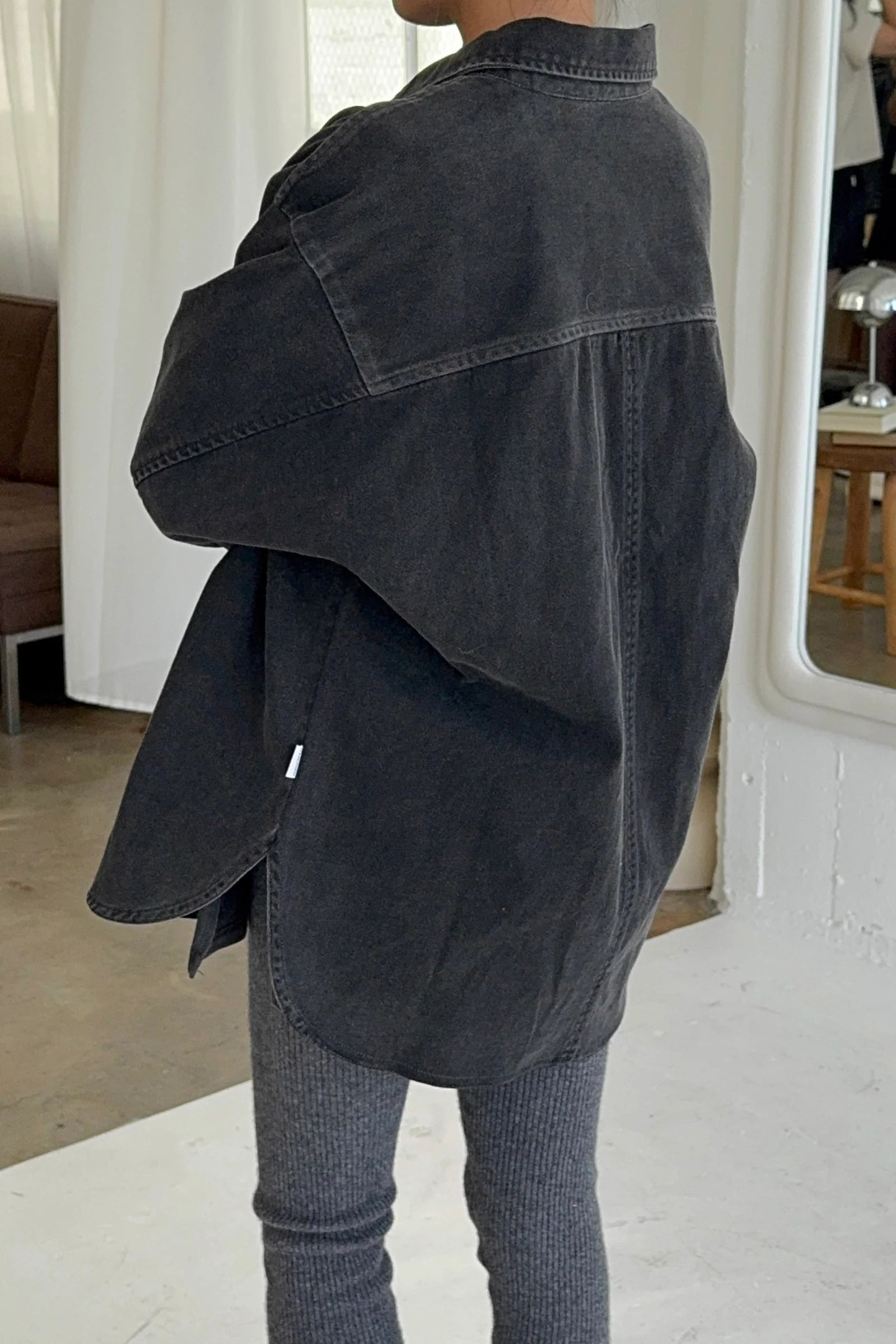 Person wearing a dark denim jacket and gray pants in an indoor setting.