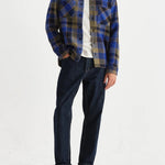 Person wearing a blue plaid shirt and dark jeans on a white background